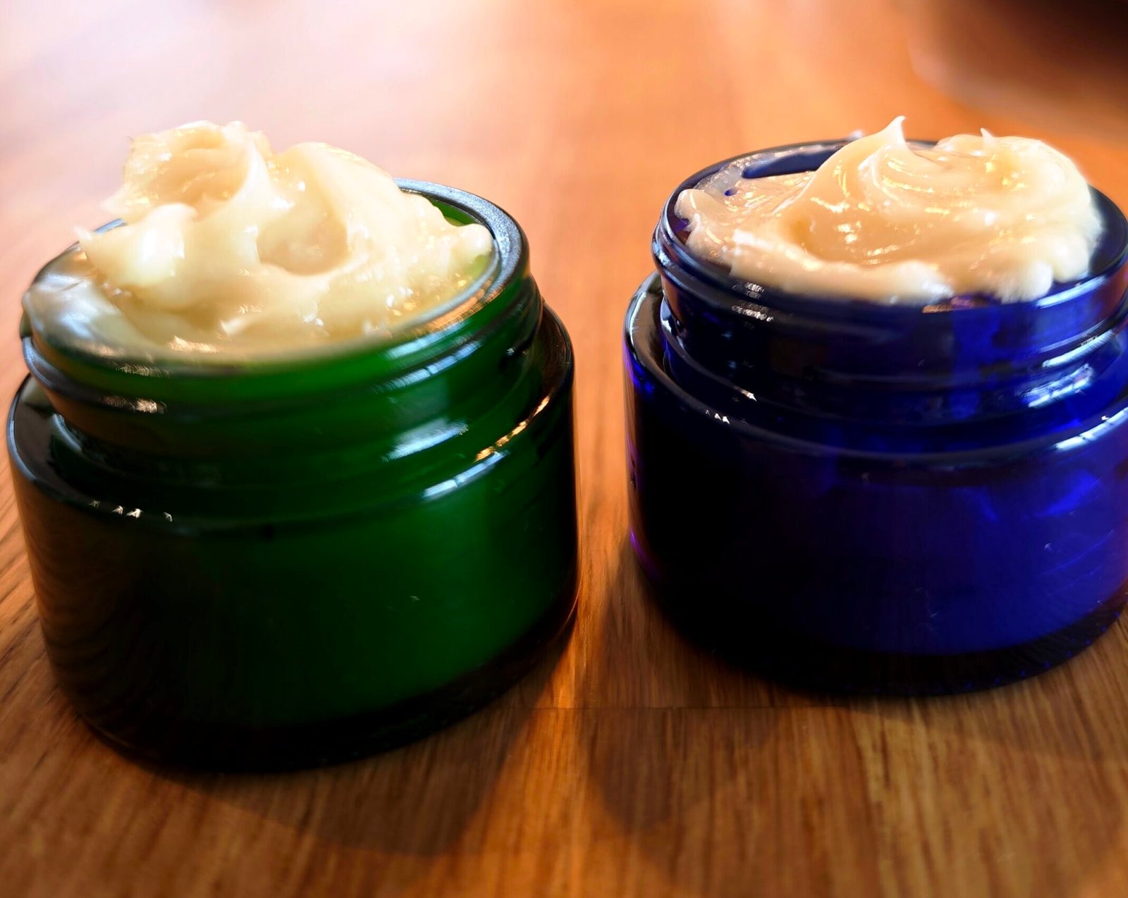 słoiczki z ciemnego szkła zielonego i niebieskiego napełnione domowym kremem